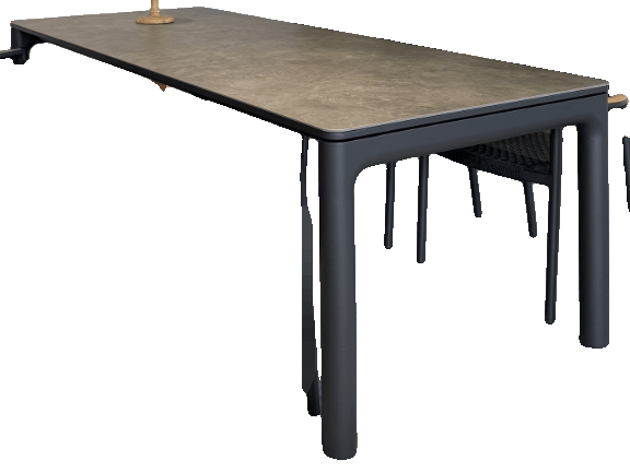 A long rectangular outdoor dining table with a dark grey top and black legs is shown with several black woven chairs around it.