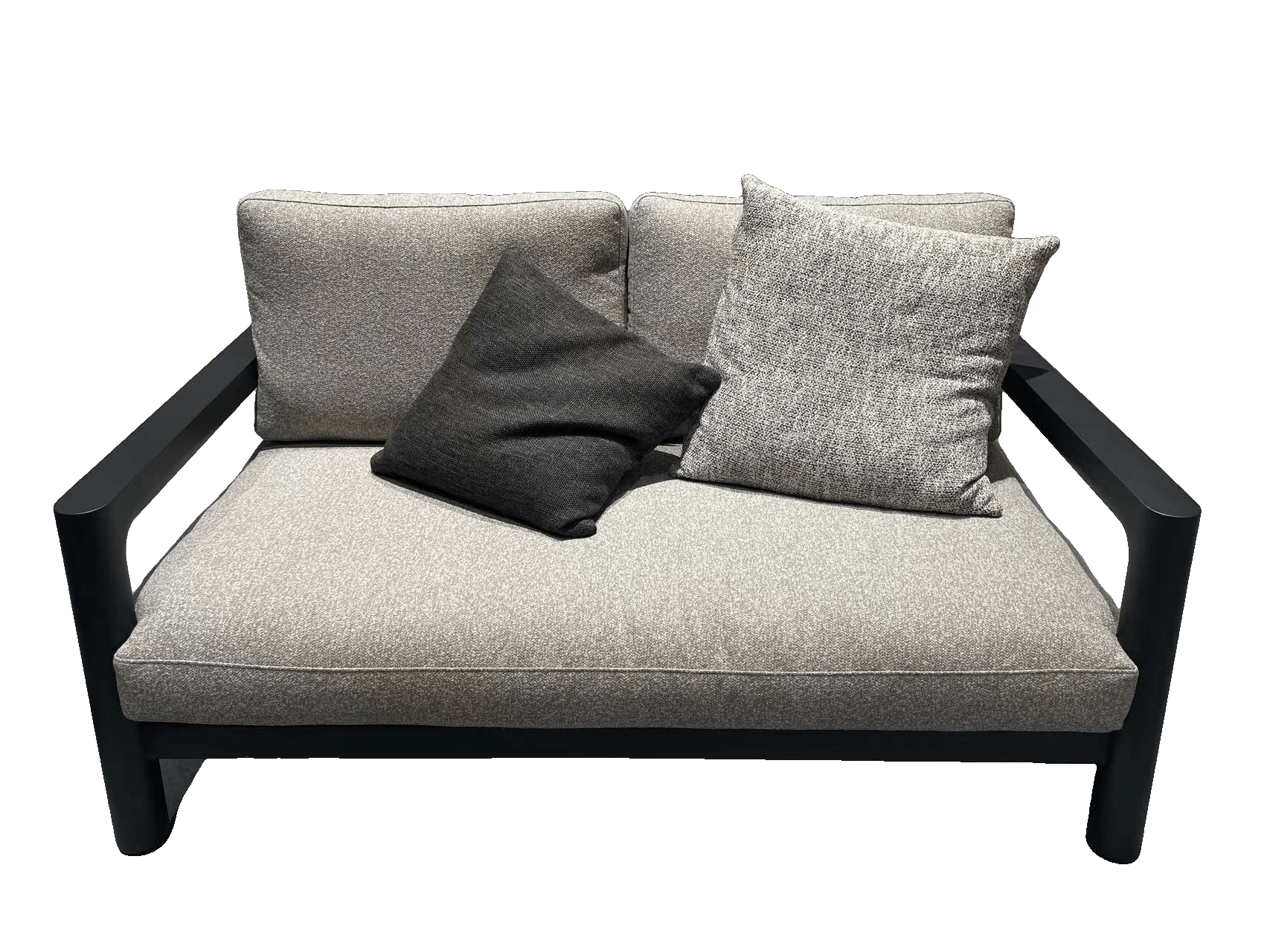 A light gray outdoor sofa with two light gray throw pillows and two dark brown throw pillows is placed on a light gray textured rug in a modern setting.